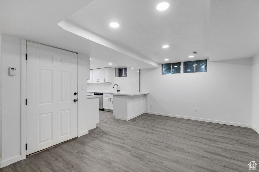 Kitchen featuring kitchen peninsula, white cabinets, stainless steel dishwasher, light hardwood / wood-style floors, and sink