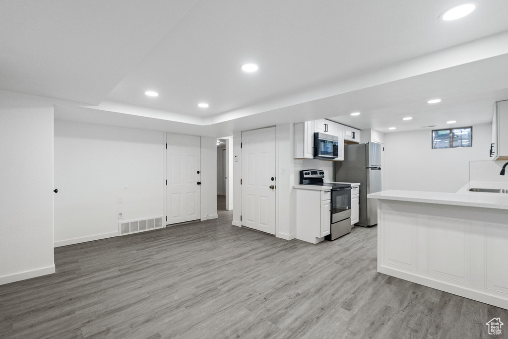 Kitchen with light hardwood / wood-style floors, appliances with stainless steel finishes, white cabinets, and sink