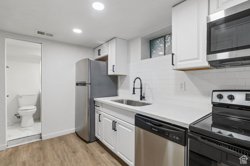 Kitchen featuring stainless steel appliances, sink, decorative backsplash, light wood-type flooring, and white cabinetry