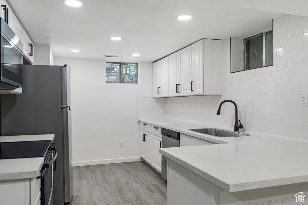 Kitchen featuring white cabinetry, light wood-type flooring, appliances with stainless steel finishes, decorative backsplash, and sink