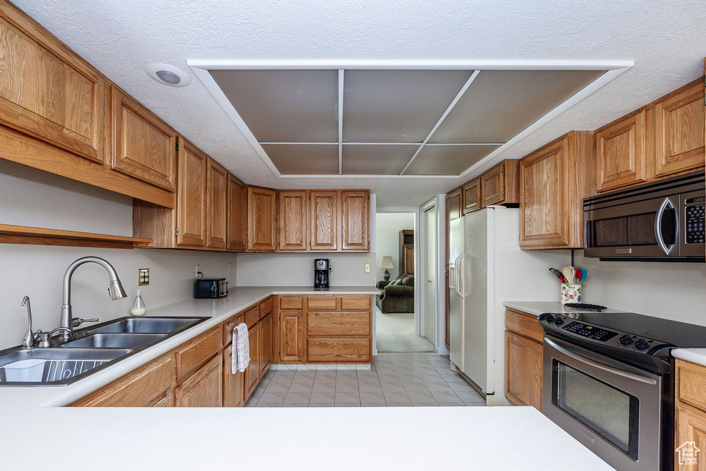 Kitchen with appliances with stainless steel finishes, a textured ceiling, light colored carpet, and sink