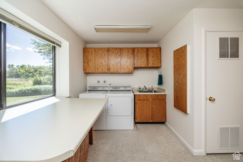 Laundry room featuring sink, separate washer and dryer, and cabinets