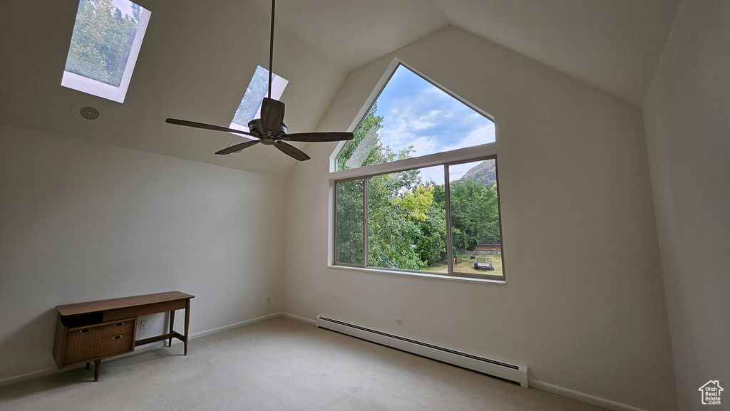 Spare room featuring a baseboard heating unit, light colored carpet, a skylight, high vaulted ceiling, and ceiling fan