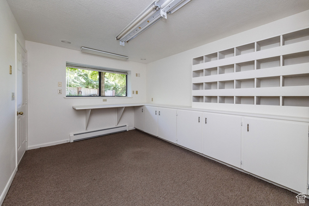 Spare room featuring a baseboard radiator, dark carpet, and a textured ceiling