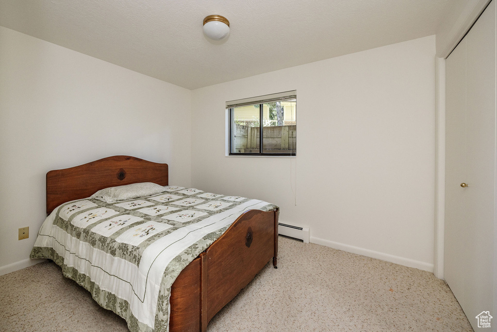 Bedroom with a baseboard radiator, a closet, and light colored carpet