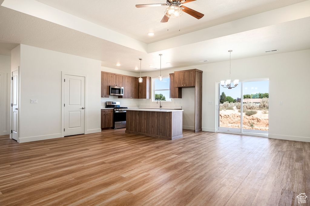 Kitchen with hanging light fixtures, a center island, light wood-type flooring, ceiling fan with notable chandelier, and stainless steel appliances