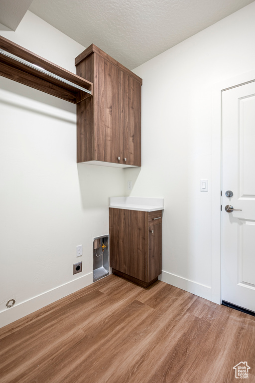 Clothes washing area featuring light wood-type flooring, hookup for an electric dryer, cabinets, and a textured ceiling