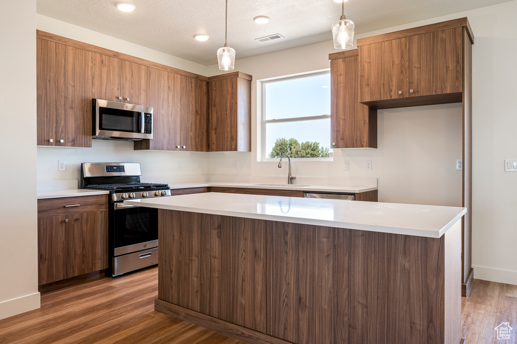 Kitchen with pendant lighting, appliances with stainless steel finishes, a center island, sink, and light wood-type flooring