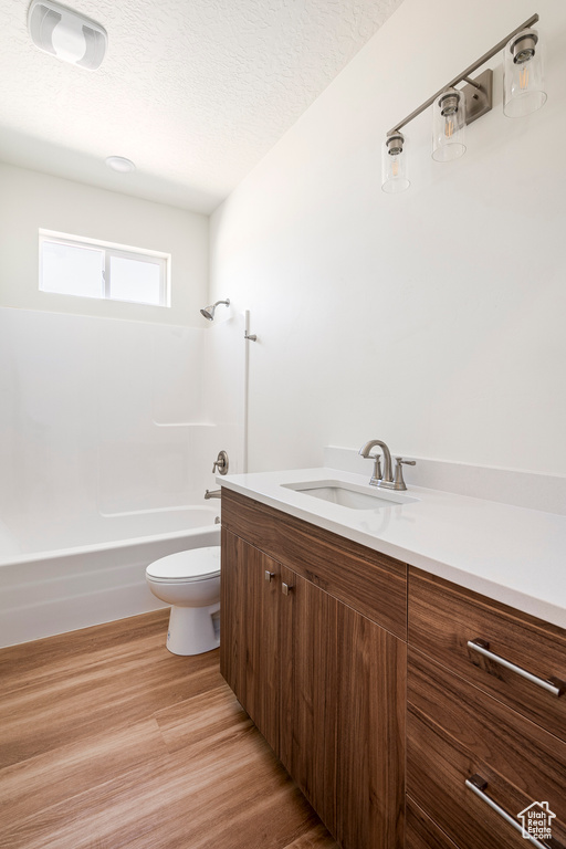 Full bathroom with a textured ceiling, vanity, hardwood / wood-style floors, toilet, and tub / shower combination