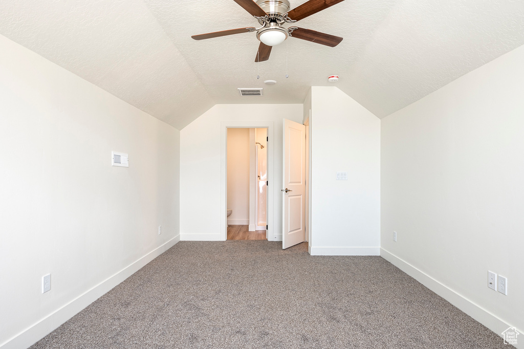 Interior space featuring a textured ceiling, light colored carpet, ceiling fan, and vaulted ceiling