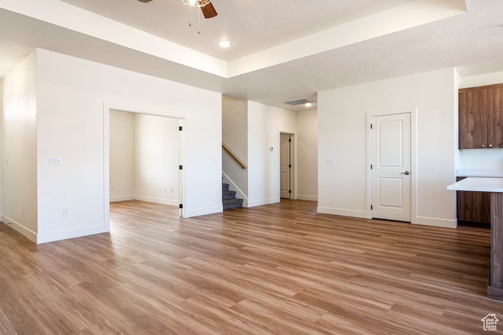 Unfurnished living room featuring light hardwood / wood-style flooring, ceiling fan, and a raised ceiling