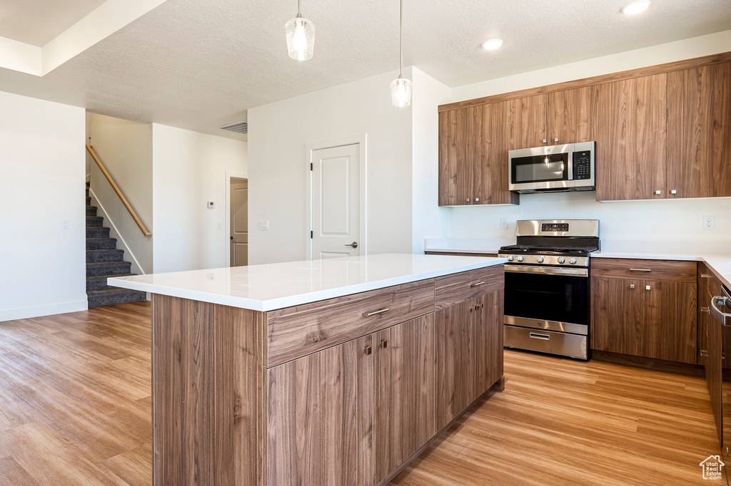 Kitchen featuring light hardwood / wood-style flooring, decorative light fixtures, appliances with stainless steel finishes, and a kitchen island