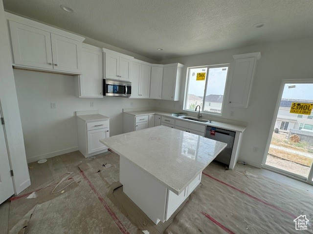 Kitchen featuring stainless steel appliances, sink, a textured ceiling, a center island, and white cabinetry