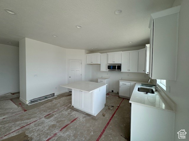 Kitchen with a center island, sink, a textured ceiling, and white cabinets