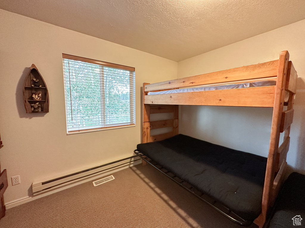 Carpeted bedroom with a baseboard radiator and a textured ceiling