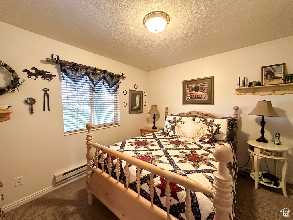 Carpeted bedroom with a textured ceiling and a baseboard heating unit