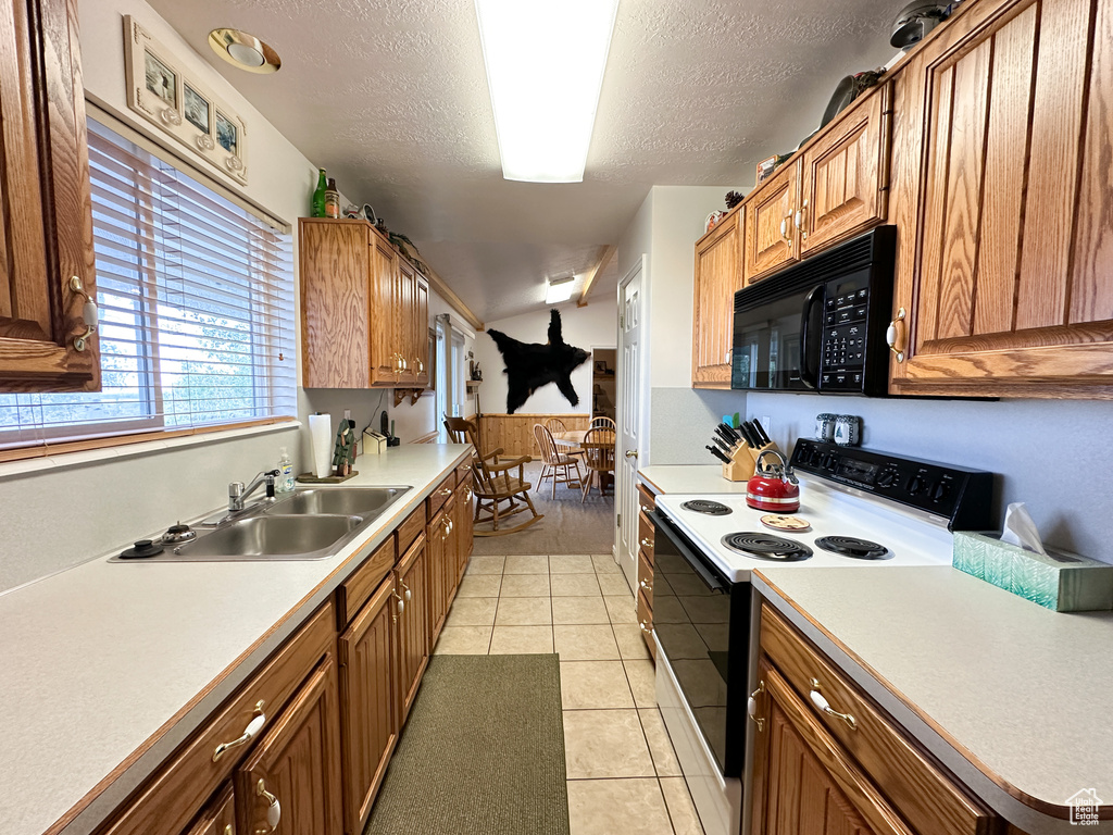 Kitchen with sink, white range with electric stovetop, a textured ceiling, and light tile patterned floors