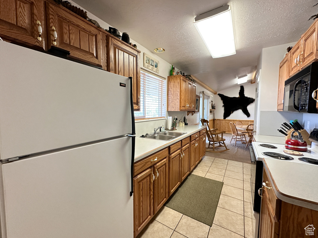 Kitchen with sink, a textured ceiling, white appliances, and light tile patterned floors