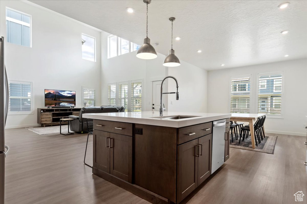 Kitchen with stainless steel dishwasher, hardwood / wood-style flooring, pendant lighting, sink, and a kitchen island with sink