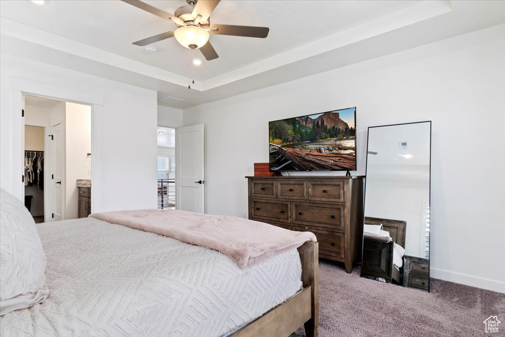 Carpeted bedroom with a raised ceiling, ensuite bath, and ceiling fan