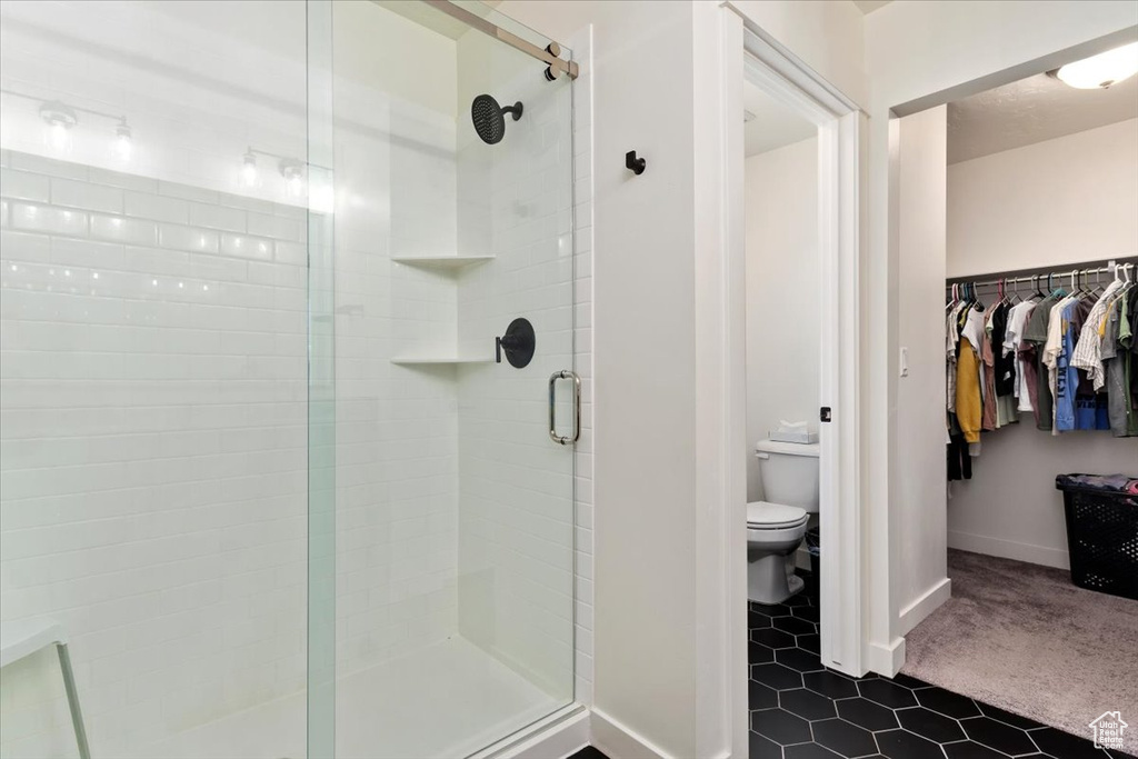 Bathroom featuring a shower with door, toilet, and tile patterned floors