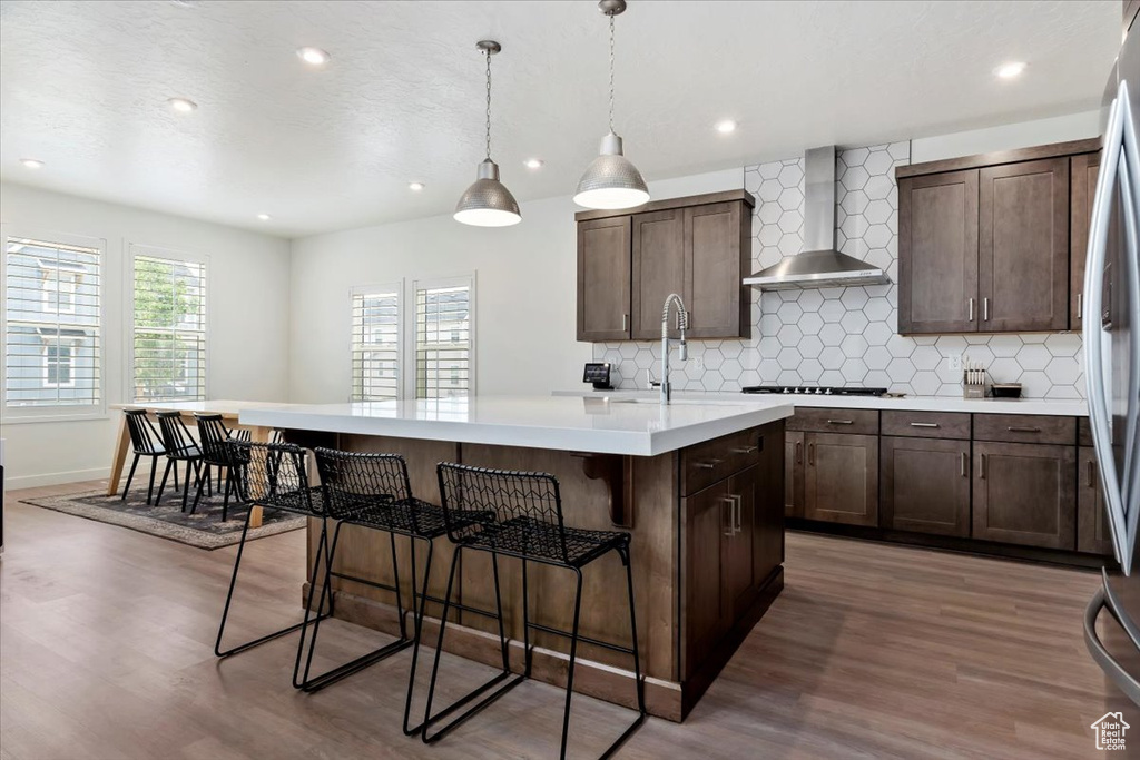 Kitchen featuring hanging light fixtures, decorative backsplash, dark hardwood / wood-style floors, a kitchen island with sink, and wall chimney exhaust hood