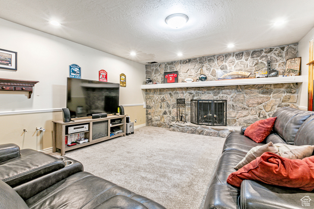 Living room featuring carpet, a textured ceiling, and a stone fireplace