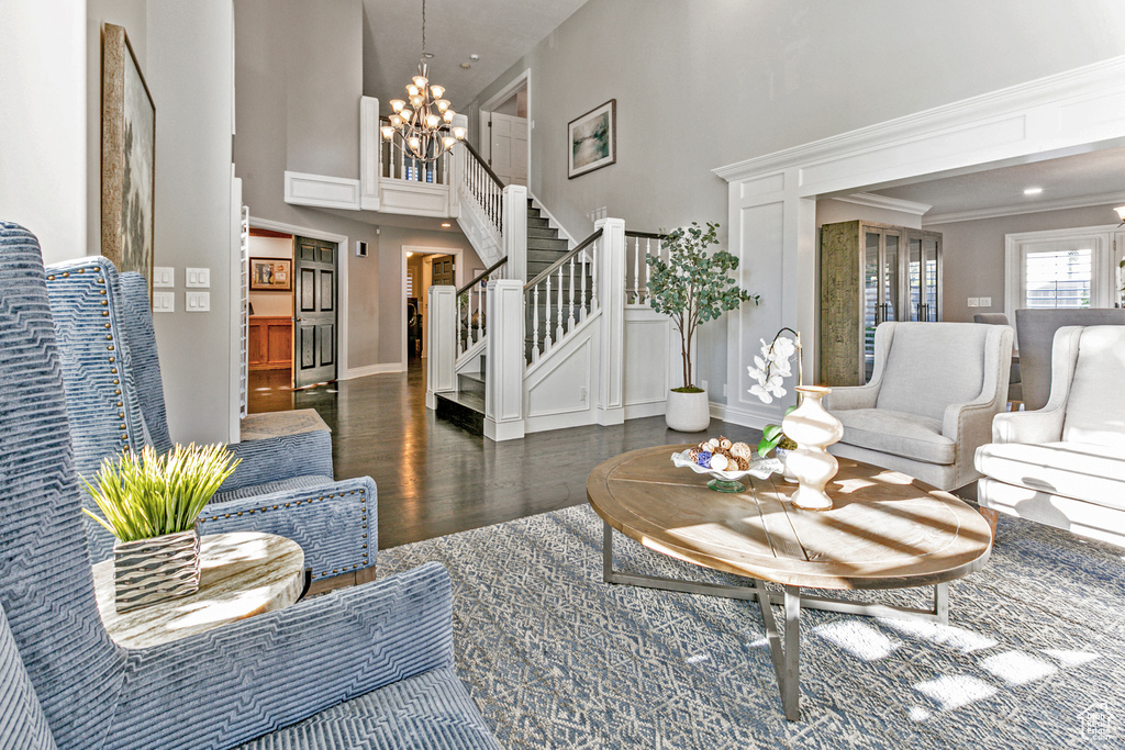 Living room with dark wood-type flooring, a towering ceiling, ornamental molding, and an inviting chandelier