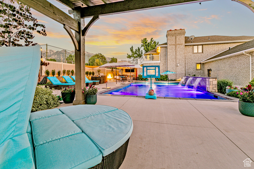 Patio terrace at dusk with pool water feature and a fenced in pool