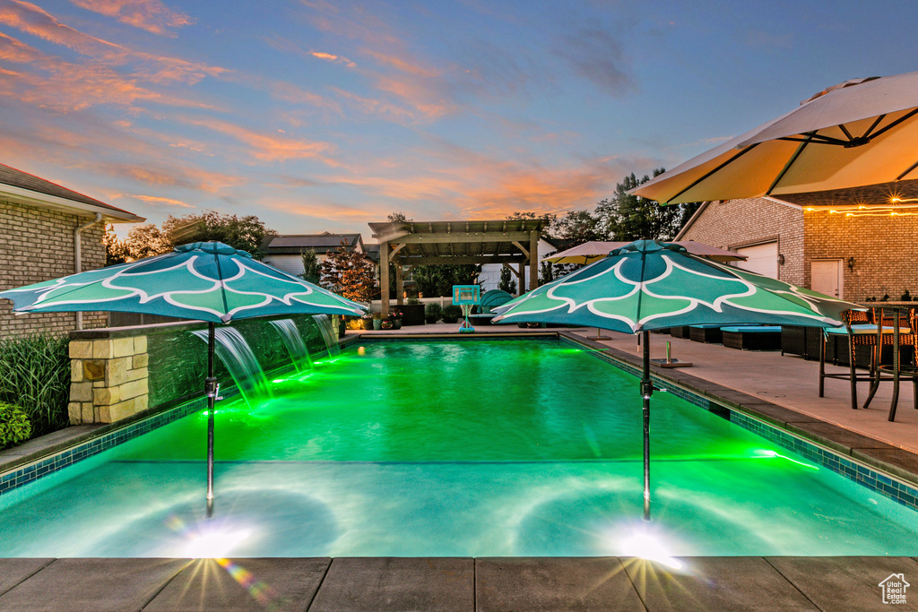 Pool at dusk with a pergola and a patio area