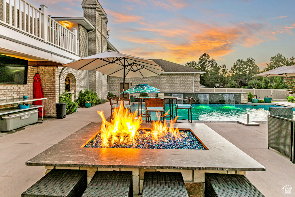 Exterior space featuring a fire pit, pool water feature, a fenced in pool, and a balcony