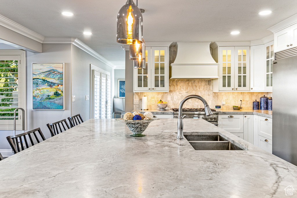 Kitchen featuring white cabinets, custom exhaust hood, tasteful backsplash, and hanging light fixtures