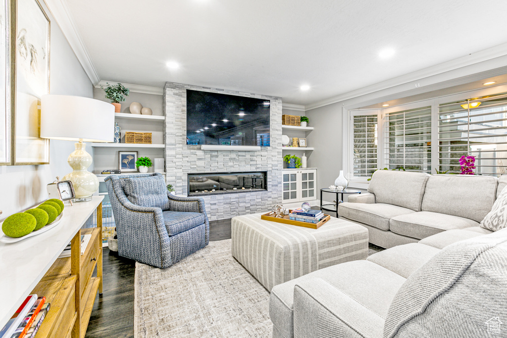 Living room featuring built in features, a stone fireplace, dark wood-type flooring, and crown molding