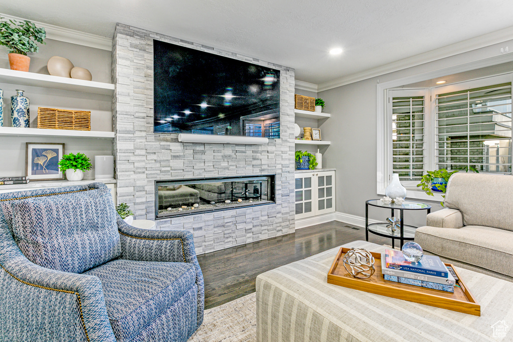 Living room featuring built in features, ornamental molding, wood-type flooring, and a fireplace