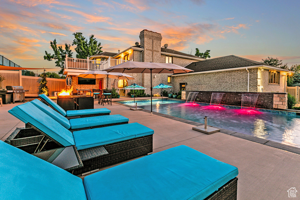 Pool at dusk featuring an outdoor living space with a fire pit, grilling area, a patio, and pool water feature