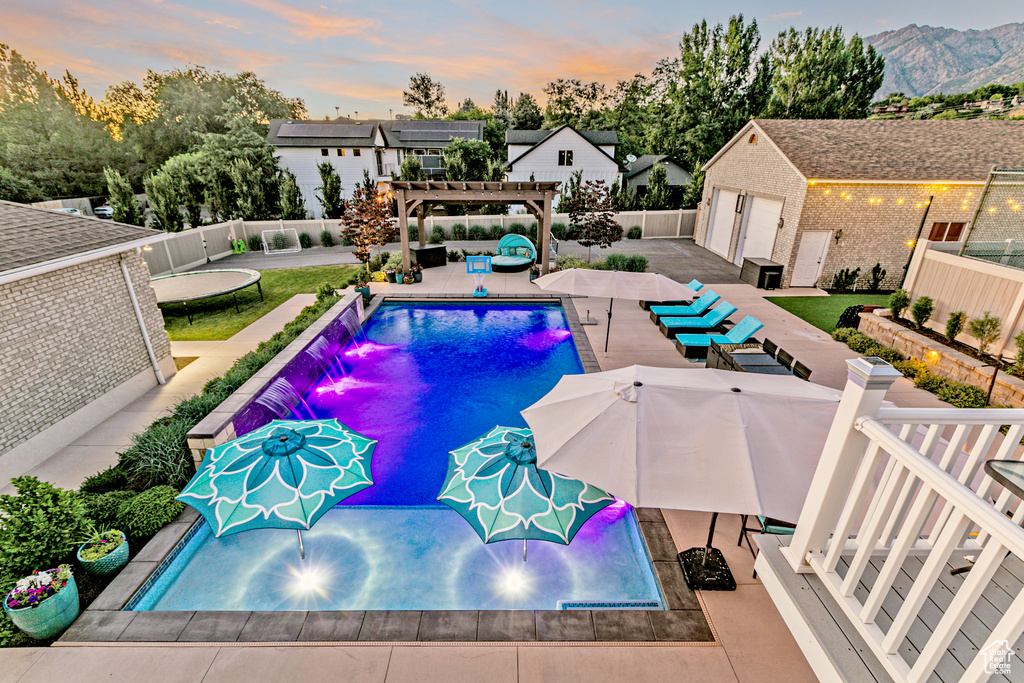 Pool at dusk with pool water feature, an outbuilding, a patio area, and a pergola