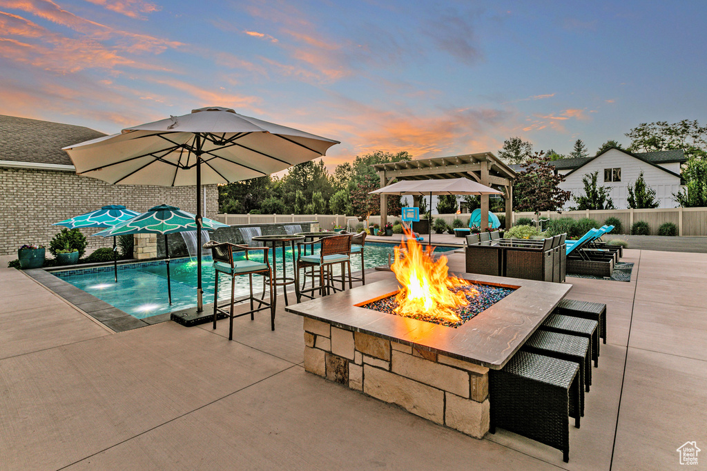 Pool at dusk featuring a patio, pool water feature, and a fire pit