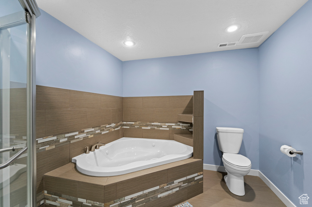 Bathroom with toilet, tiled bath, and tile patterned flooring