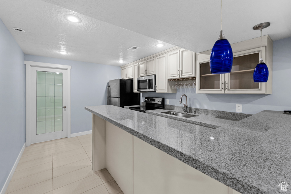 Kitchen with stainless steel appliances, white cabinets, sink, hanging light fixtures, and stone countertops