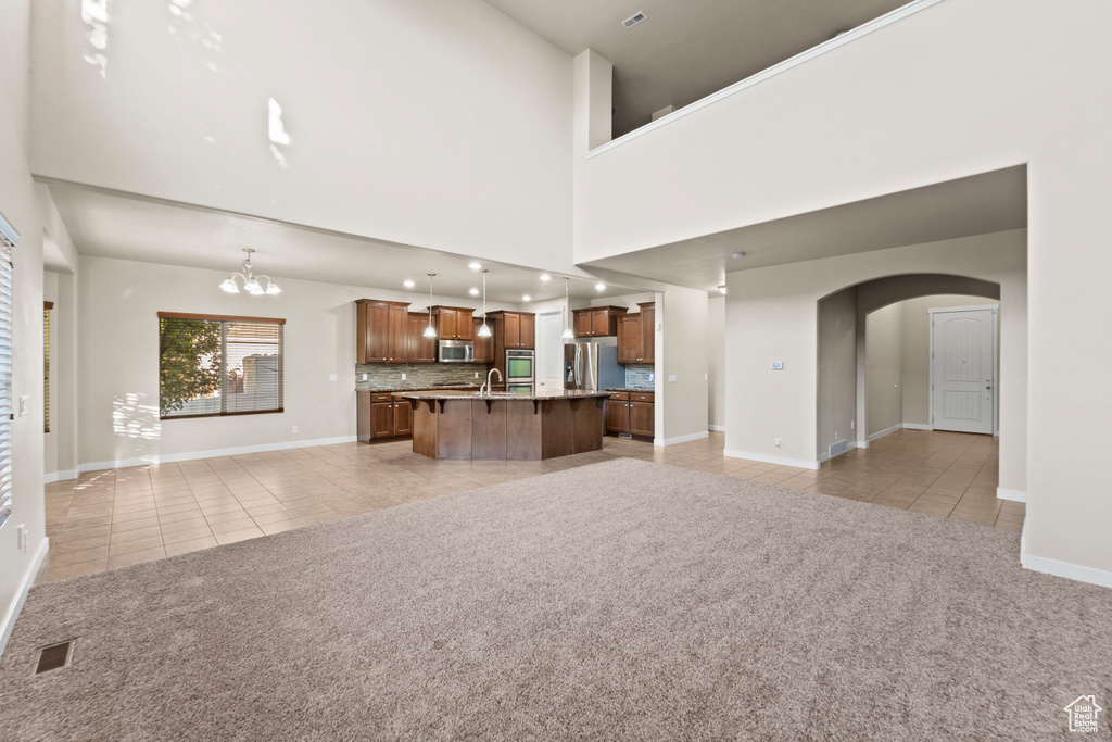 Unfurnished living room featuring light tile patterned flooring, a towering ceiling, sink, and a chandelier