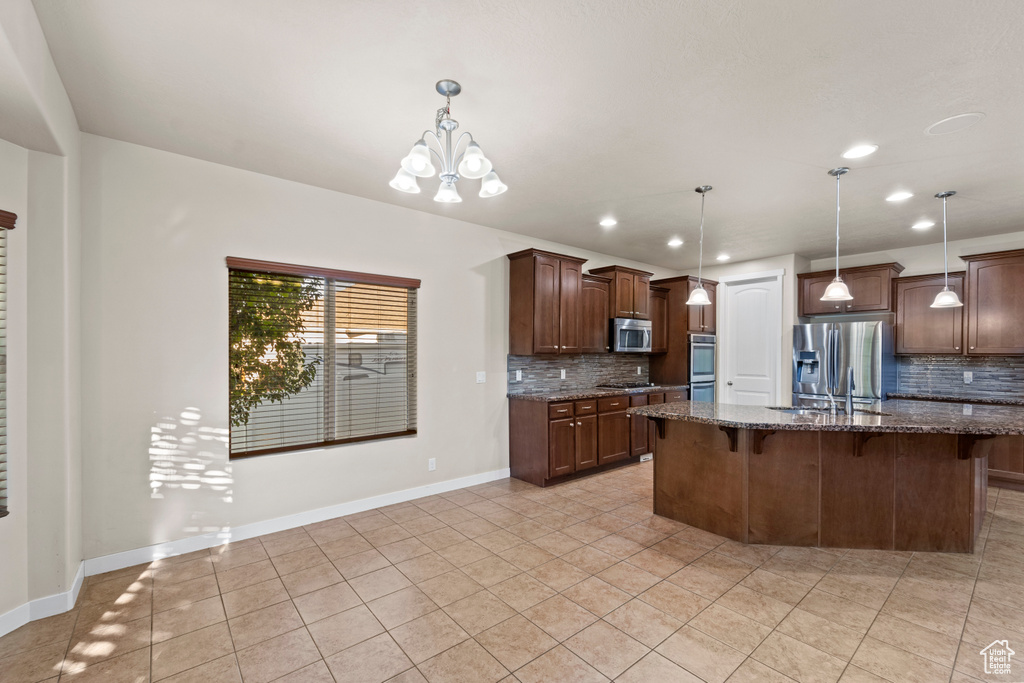 Kitchen with appliances with stainless steel finishes, pendant lighting, decorative backsplash, and dark stone counters