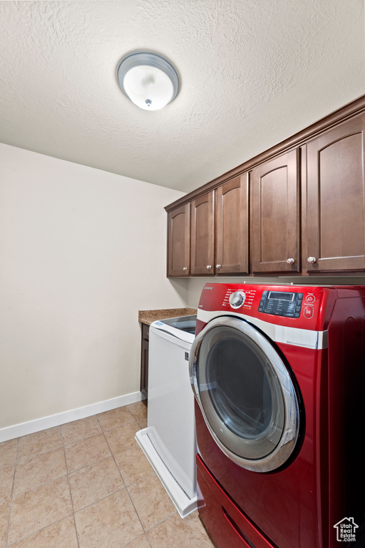 Laundry area featuring light tile patterned flooring, independent washer and dryer, cabinets, and a textured ceiling