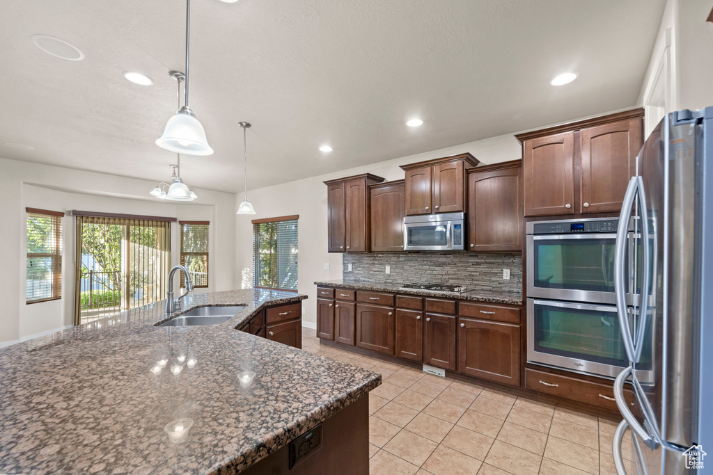 Kitchen with dark brown cabinets, appliances with stainless steel finishes, decorative backsplash, pendant lighting, and sink