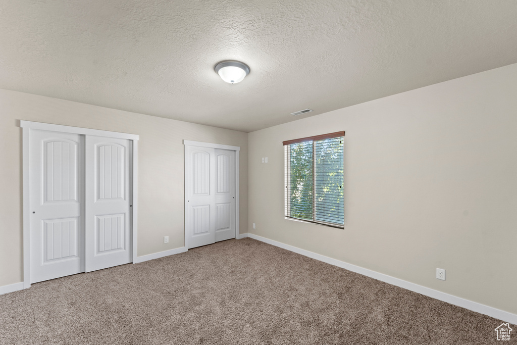 Unfurnished bedroom with carpet flooring, a textured ceiling, and two closets