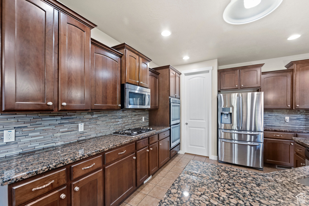 Kitchen featuring decorative backsplash, dark brown cabinets, light tile patterned flooring, and appliances with stainless steel finishes