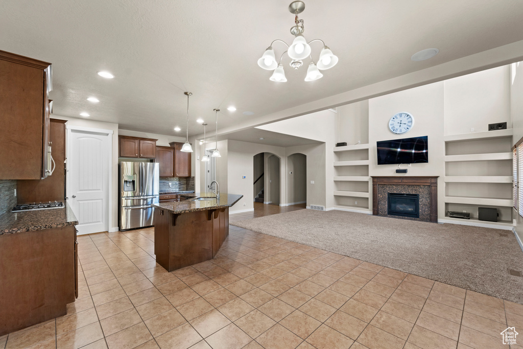 Kitchen with tasteful backsplash, built in shelves, stainless steel appliances, a tiled fireplace, and decorative light fixtures