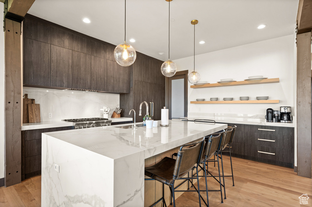 Kitchen with a kitchen breakfast bar, an island with sink, dark brown cabinets, light hardwood / wood-style flooring, and decorative light fixtures