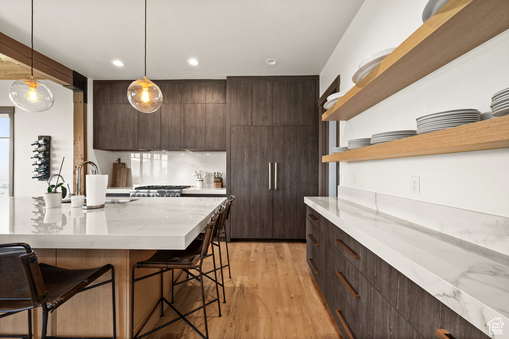 Kitchen with an island with sink, hanging light fixtures, sink, light hardwood / wood-style flooring, and a kitchen breakfast bar