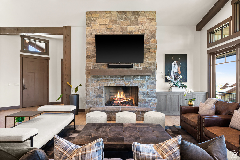 Living room with wood-type flooring, vaulted ceiling with beams, and a stone fireplace