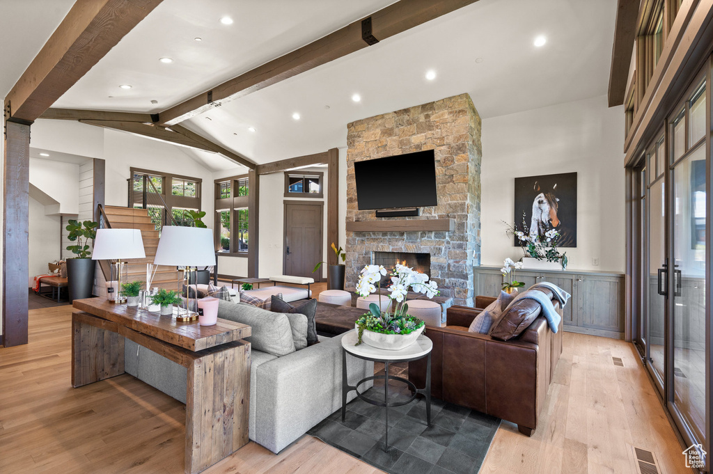 Living room with vaulted ceiling with beams, a stone fireplace, and light hardwood / wood-style flooring